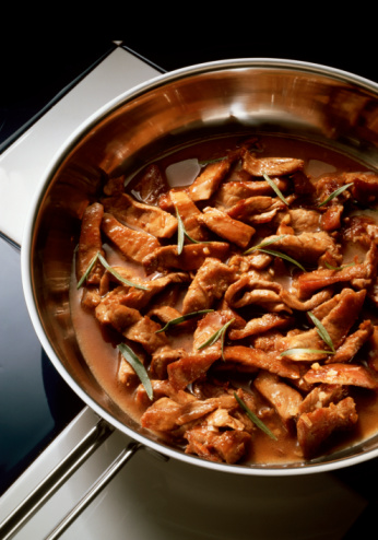 a silver pan with brown cooked lamb in a brown sauce, abbacchio alla romana