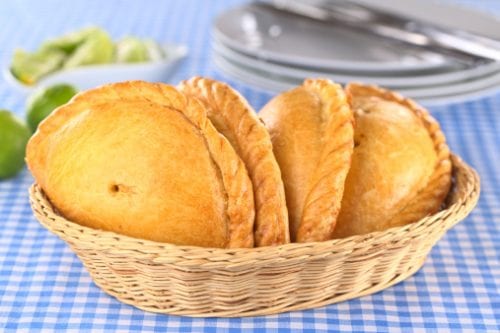 a straw basket of golden brown empanadas saltenas on a blue and white checked table