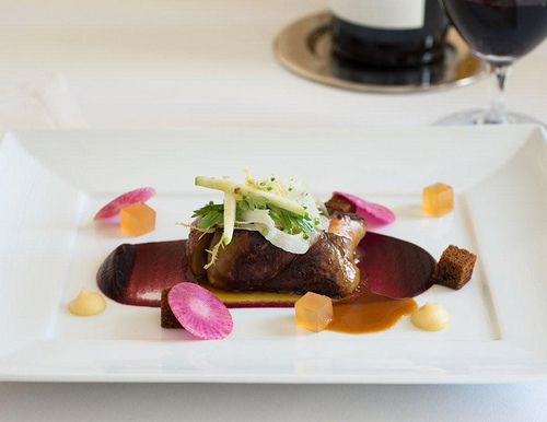 foie gras on a white plate topped with green leaves and pink and yellow fruit chunks