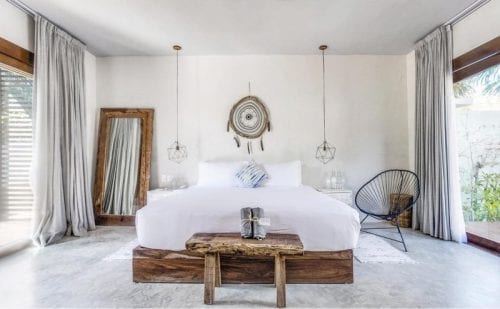 A white bedroom with white and wood furnishings and two large windows on each side