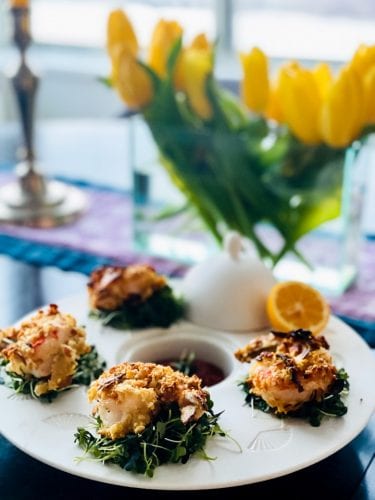 golden shrimp on green leaves on a white plate against a backdrop of yellow tulips