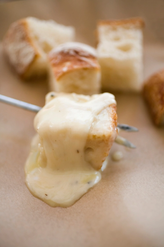 cubes of white bread covered in yellow cheese sauce on a silver fondue fork