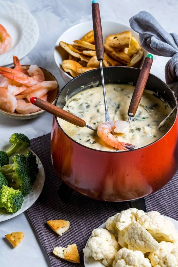 white bowls of food on a grey table around a red bowl of cheese fondue