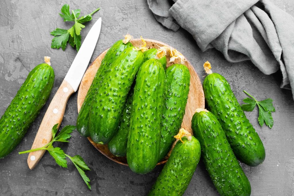 looking down on a plate full of green cucumbers and a wooden knife set on a grey tablecloth