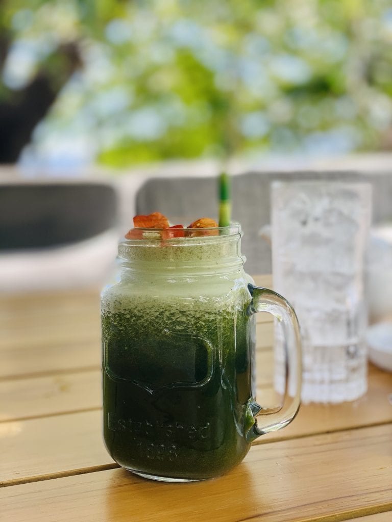 a glass of green juice and ice with an orange garnish on a brown wood table top