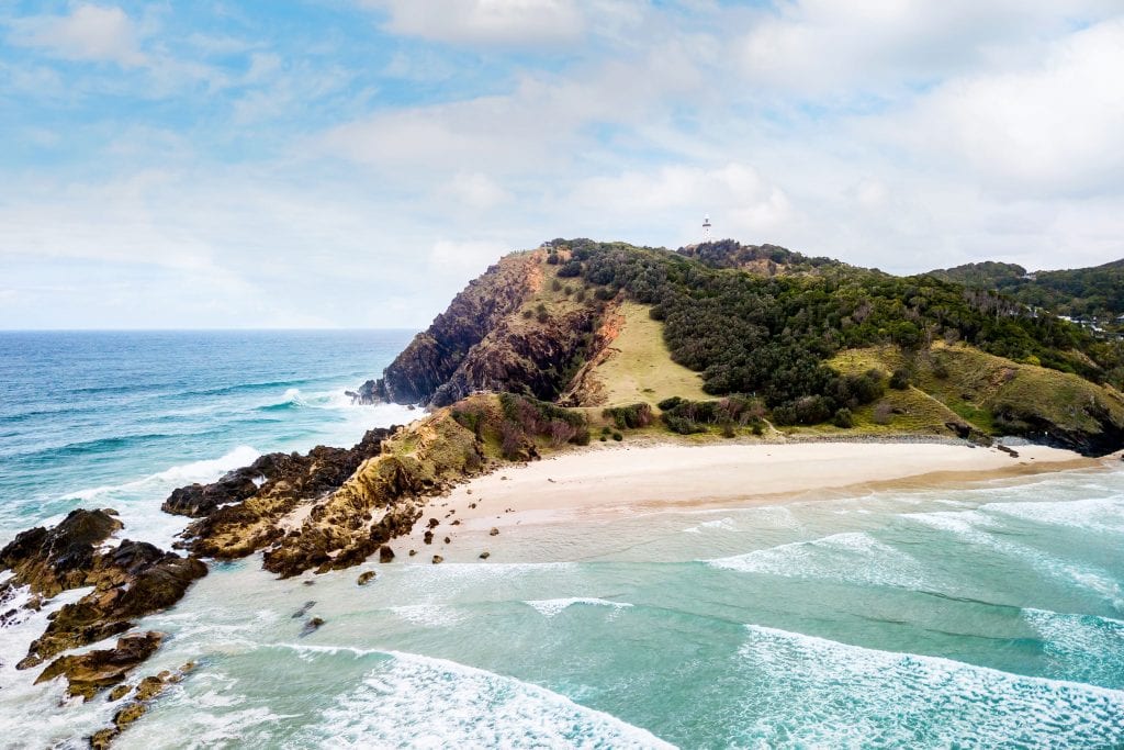 a yellow sandy beach backed by a green hill against a blue sea and blue sky, Byron Bay 