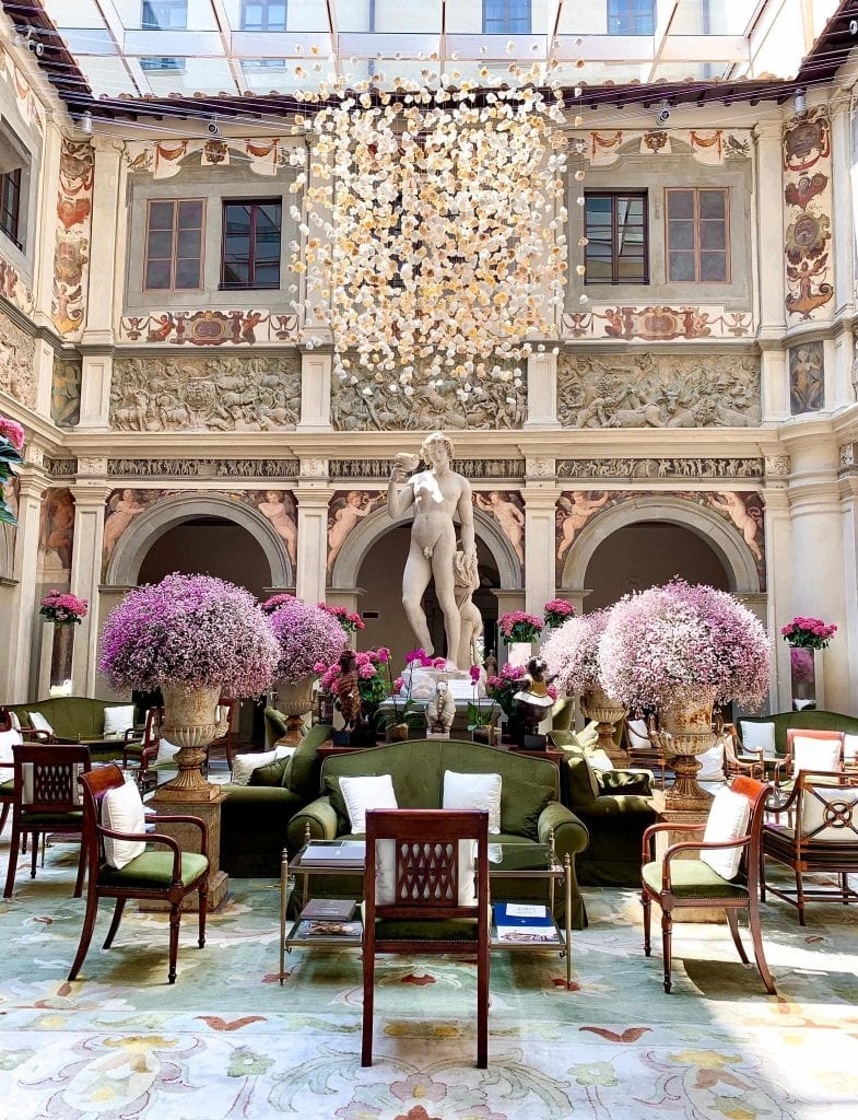 a hotel interior with a glass ceiling, a dangling chandelier, purple plants, green sofas and red chairs. Best Four Seasons in the world
