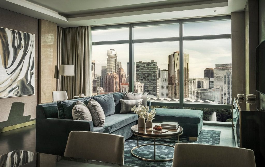 hotel room interior with green sofas, black and white wall art, large glass windows showing a skyscraper backdrop