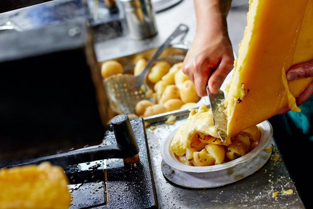 top layer of raclette is being scraped over potatoes in a traditional swiss raclette meal