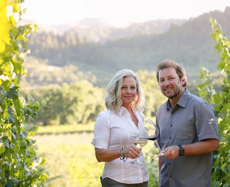 Philippe and Cherie Melka each holding a glass of wine in the vineyard.