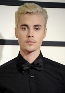 man with short blond hair in a black suit against a white backdrop