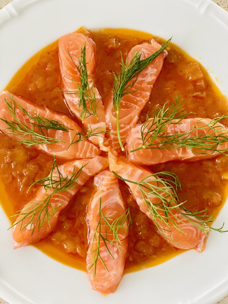 looking down onto a white plate of food containing orange sauce, green leaves, raw pink salmon