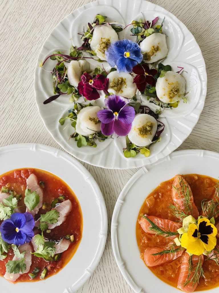 three white plates on a white table with brown sauce and purple, blue and yellow flowers
