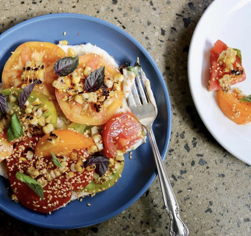 Red and orange tomato salad on a blue plate with a silver fork.