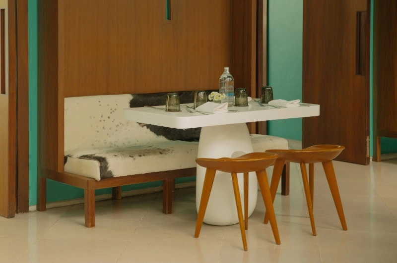 brown wooden stools at a white table laid for dinner against a white and brown bench