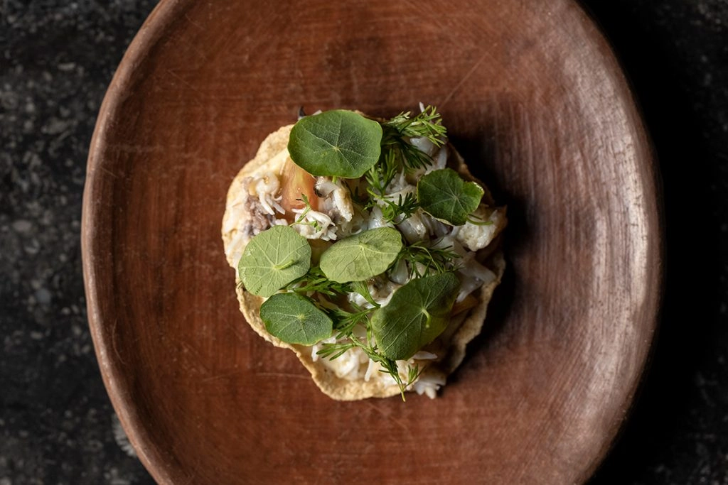 looking down onto food topped with green leaves in a brown wooden bowl