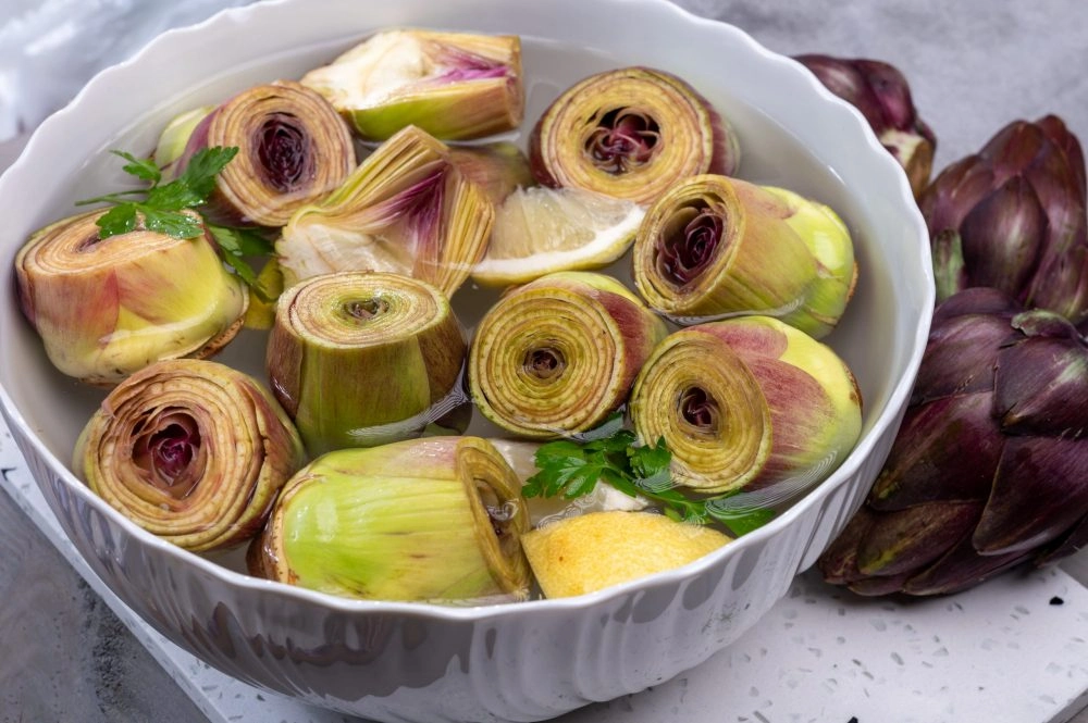 White bowl with lemon water and hearts of fresh purple romanesco artichoke vegetables close up