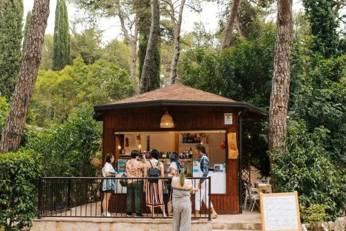 A small wooden cheese kiosk in a lush Italian forest with guests gathered outside ordering food at Baby Dicecca in Puglia