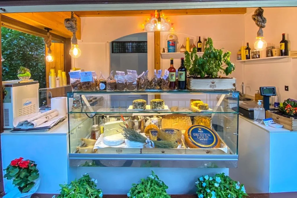 Interior cheese counter displaying artisan cheeses, wine bottles, and fresh ingredients at Baby Dicecca restaurant in Italy